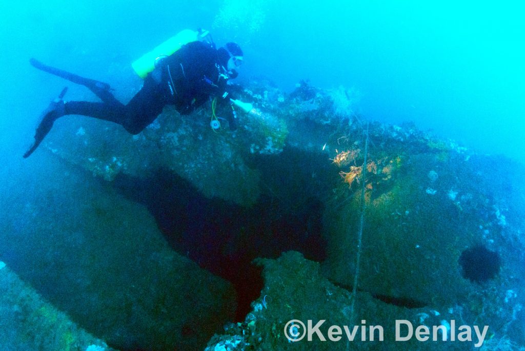 A large shell hole can been seen in the port upper hull just below the aft superstructure. The diver is holding on to the port deck edge, while in lower left can be seen the upper edge of the armour belt.