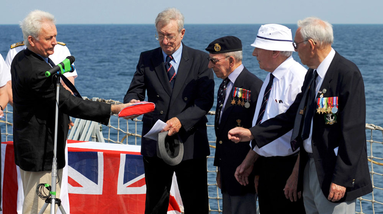 As part of the memorial service - on behalf of the wreck discovery dive team - exploration diver Kevin Denlay hands over the Royal Navy Ensign that was ‘flown’ on the wreck of HMS Exeter - upon its discovery in 2007 - to four surviving veterans of Exeter’s sinking.